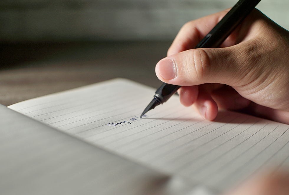 an open journel, mostly blank, with a hand and a pen starting to write